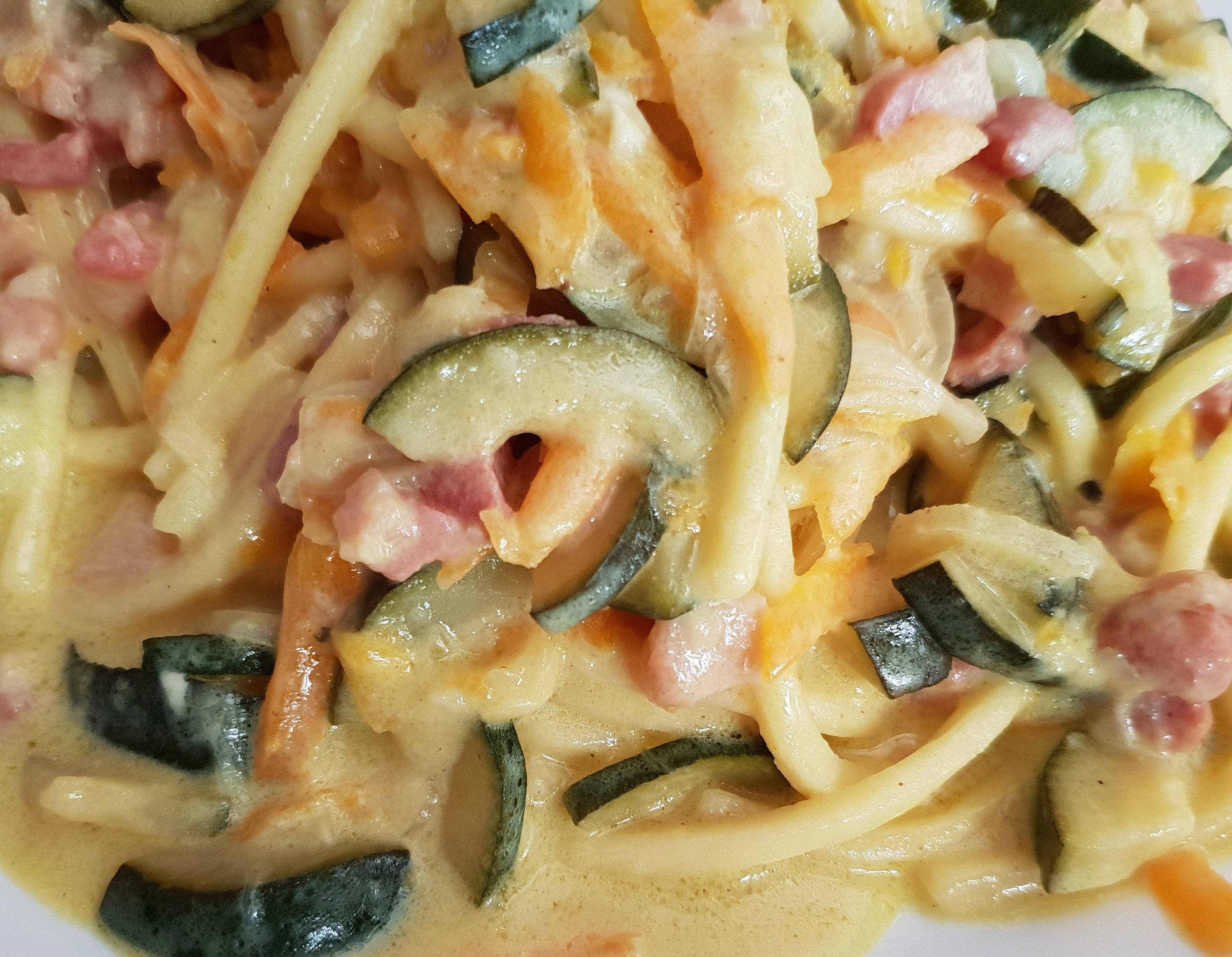 A close-up of a creamy pasta dish with zucchini and ham.