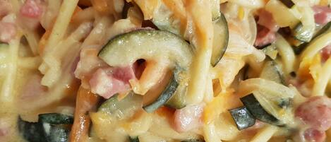 A close-up of a creamy pasta dish with zucchini and ham.