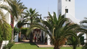 A courtyard with palm trees, a white building with a bell tower, and a clear blue sky. - Apartamentos Torrelaguna (Vera)