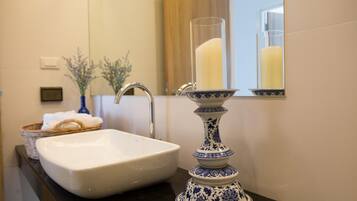 Un baño con un lavabo blanco, un florero azul y blanco, y un espejo que refleja una vela.