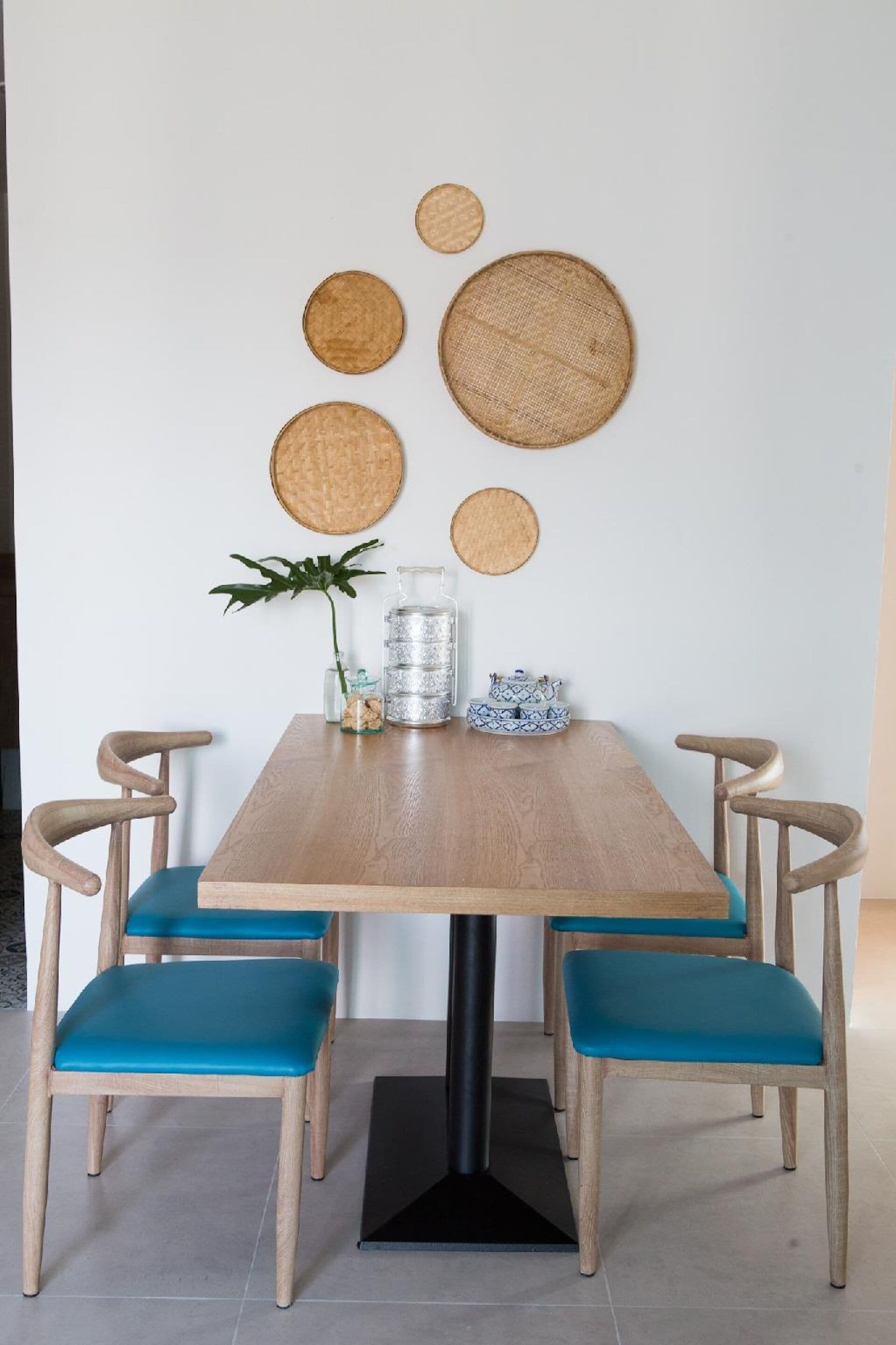 A dining table with four chairs, a plant, a metal pitcher, and decorative woven circles on the wall.
