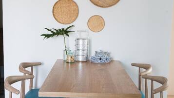 A dining table with four chairs, a plant, a metal pitcher, and decorative woven circles on the wall.