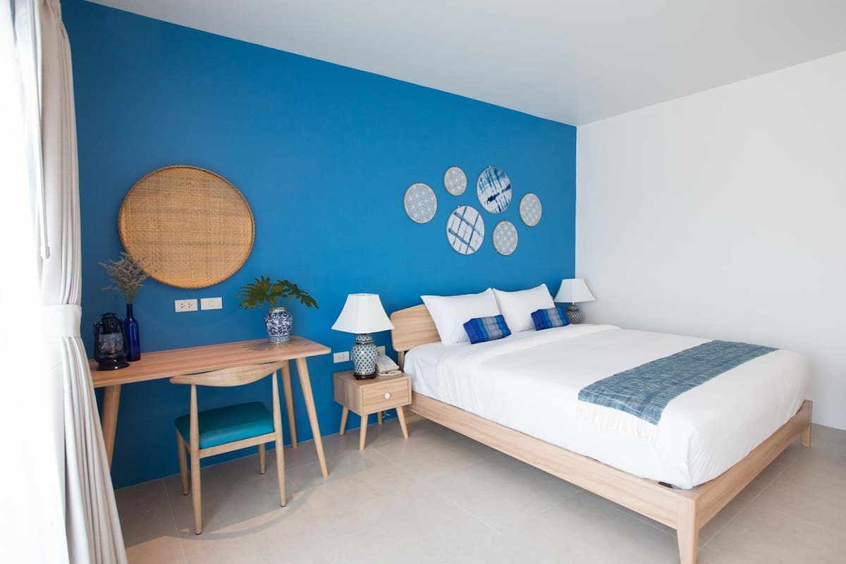 A modern bedroom with a blue accent wall, a wooden bed, a desk with a chair, and a nightstand with a lamp.