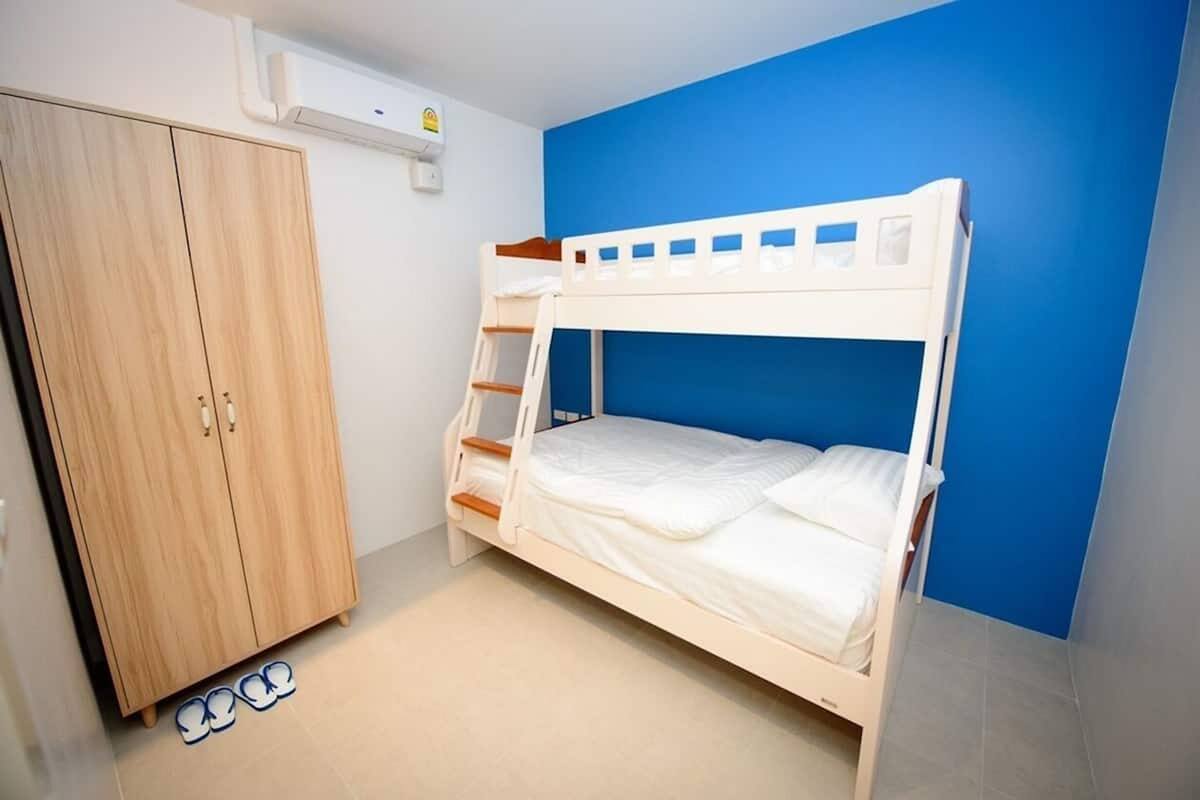 A bunk bed with a blue wall, a wooden wardrobe, and a pair of slippers on the floor.