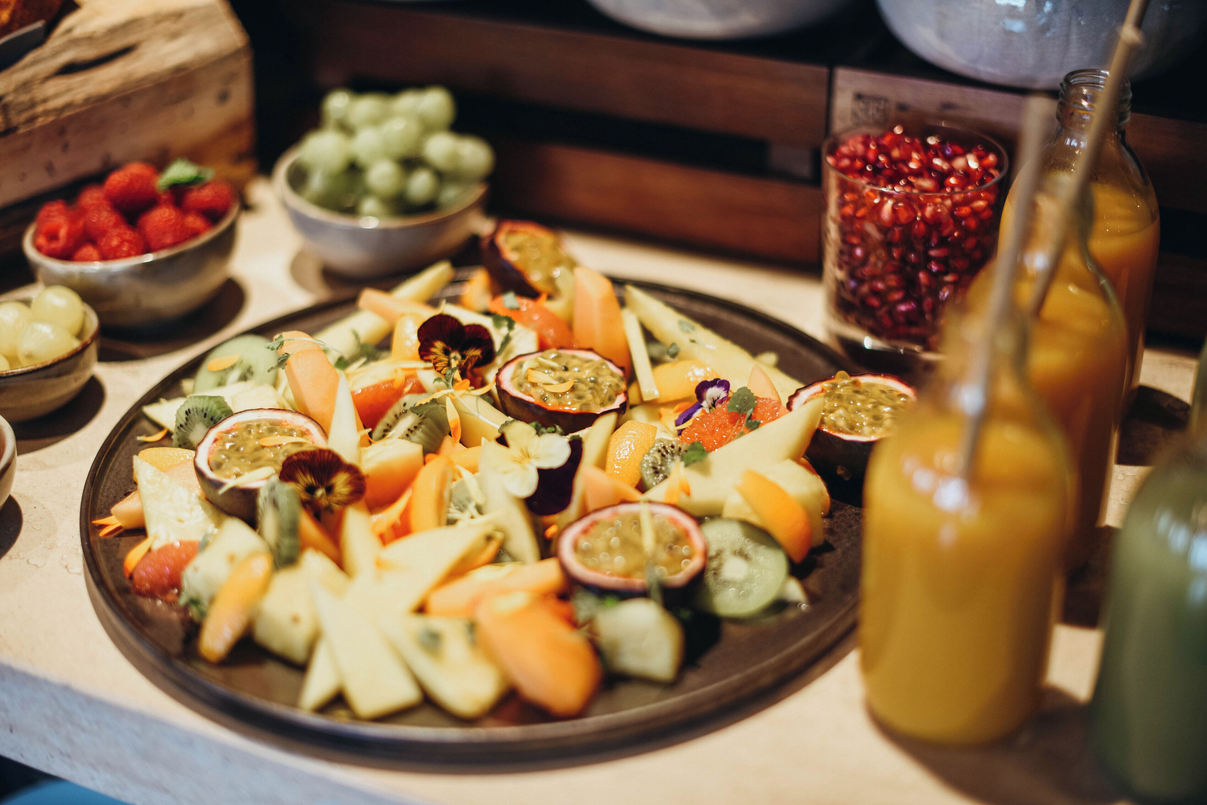 Een schaal met diverse soorten fruit en een fles sap op een tafel.