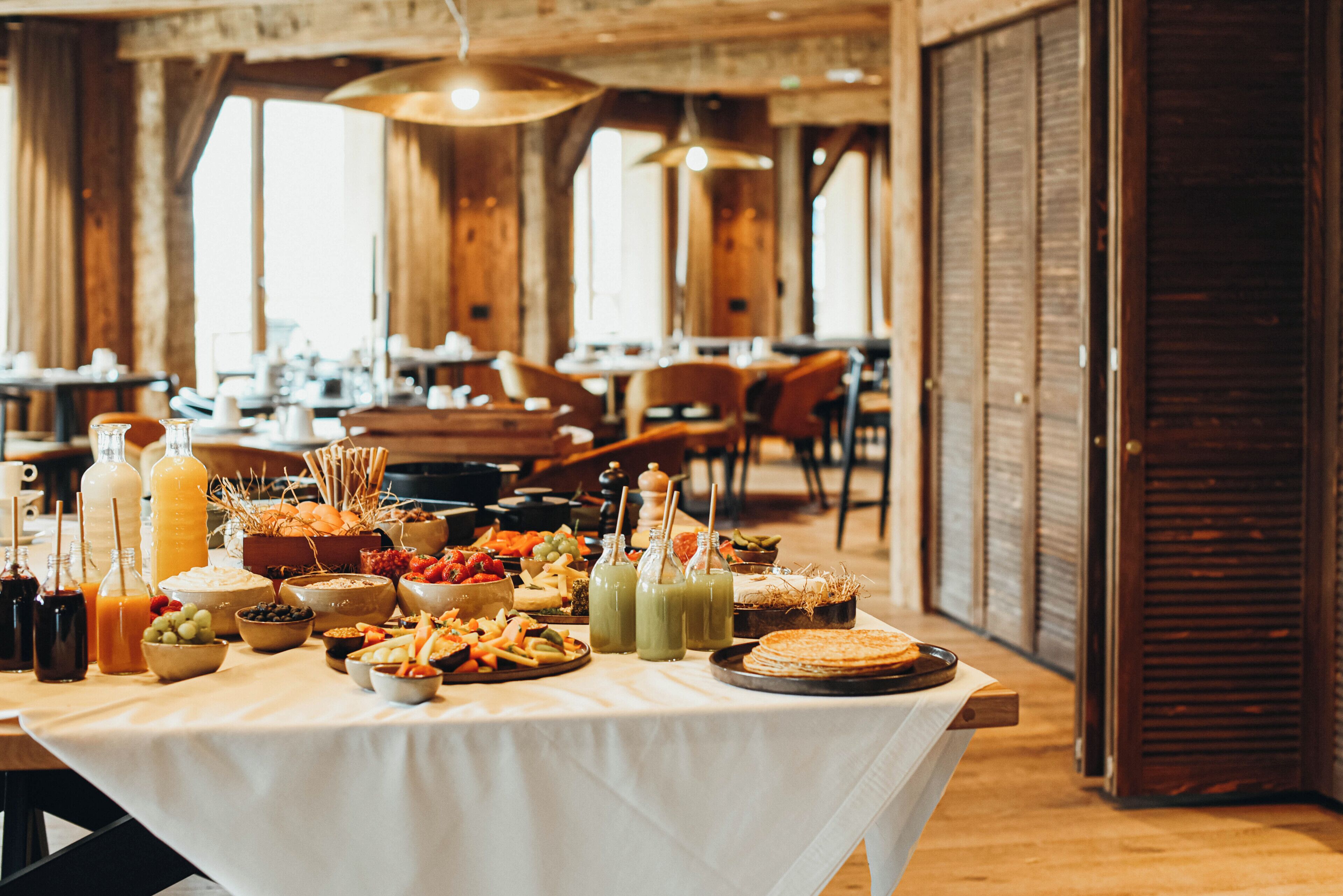 Une table de buffet garnie de divers plats et boissons, installée dans une pièce aux murs en bois et aux grandes fenêtres.