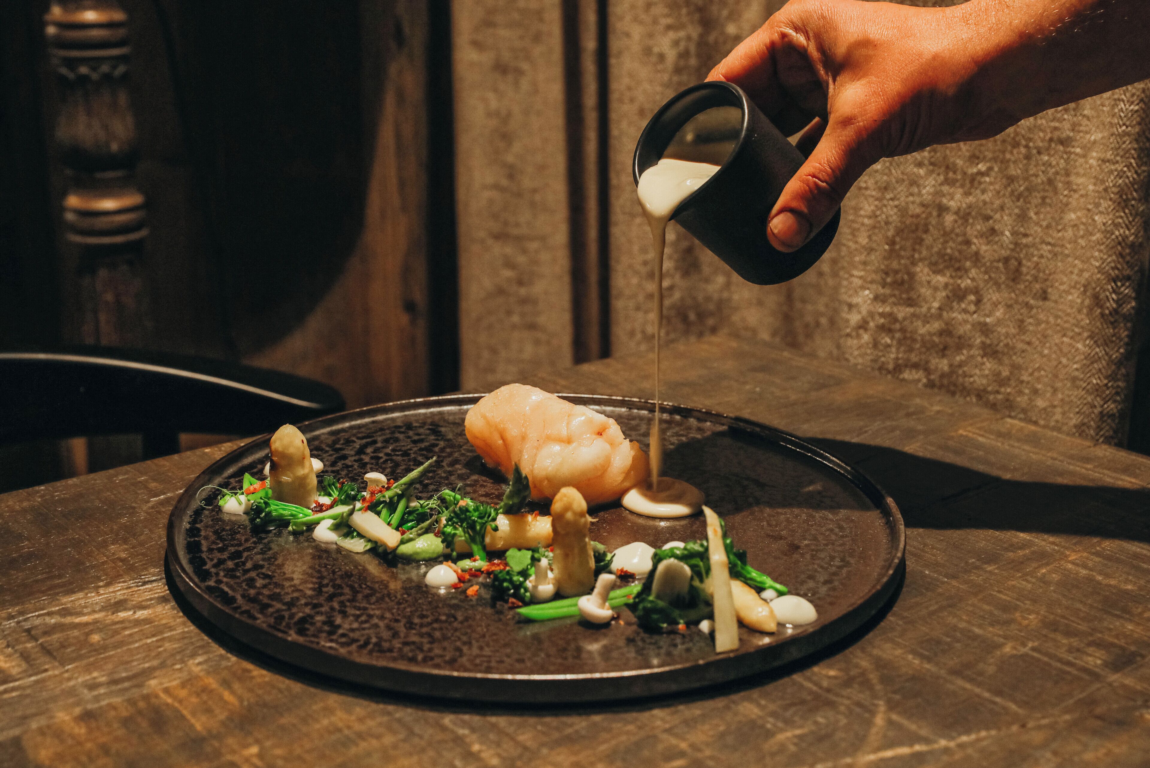 A hand pouring sauce onto a plate of food.
