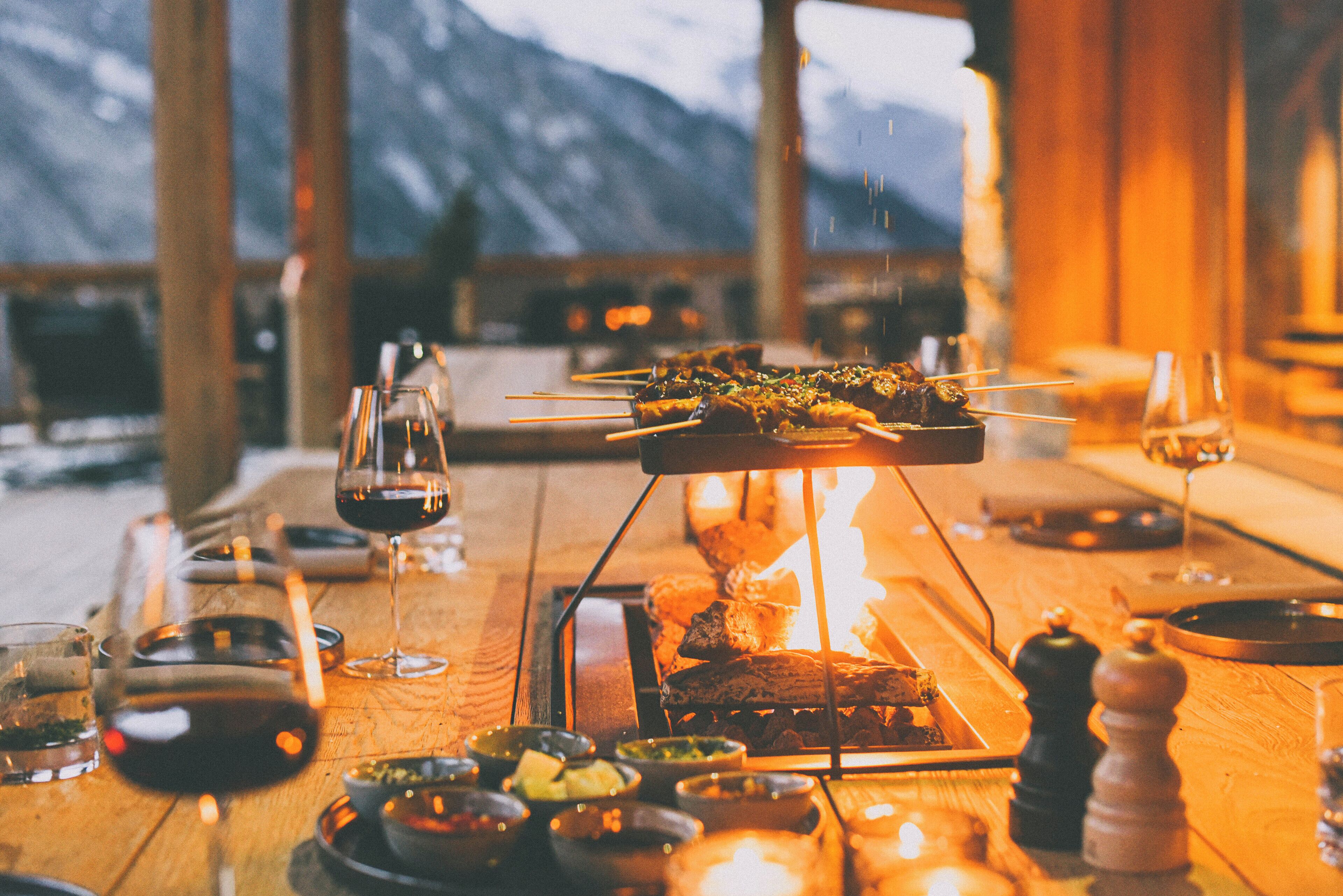 A dining table with skewers of food, wine glasses, and small bowls of condiments.