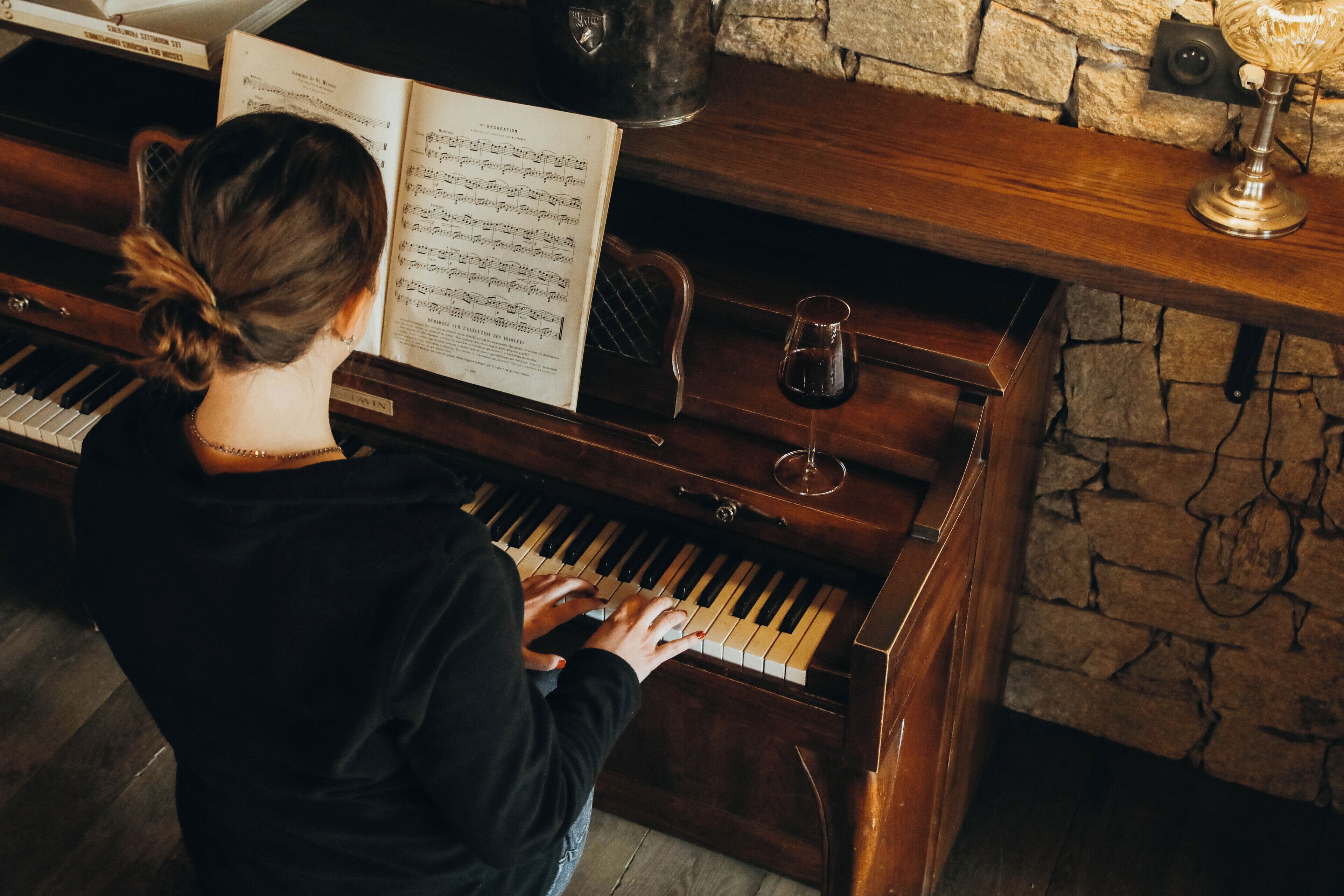Una persona tocando el piano con partituras abiertas delante.
