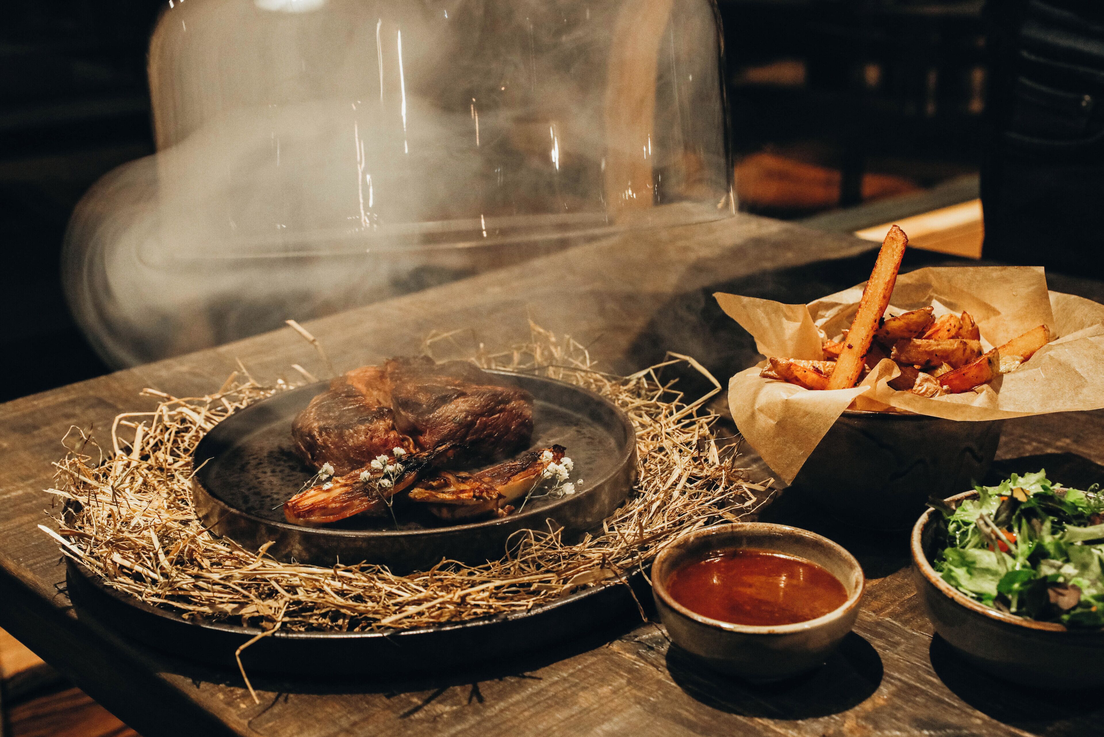 A dining table with a roasted chicken, fries, and a salad.