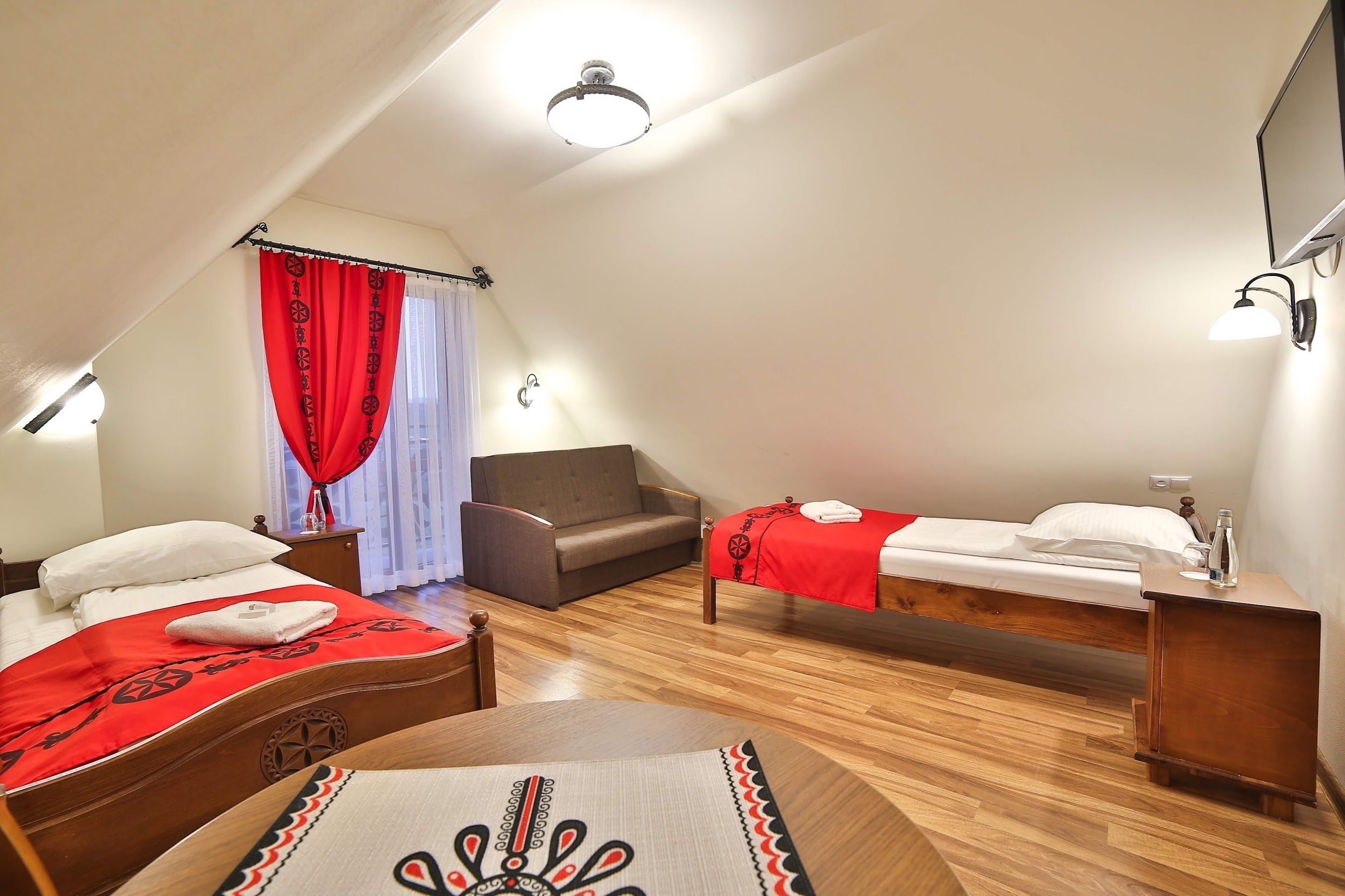 A room with two beds, a sofa, a wooden table, and a ceiling light fixture.