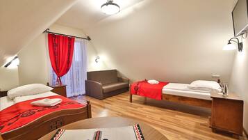 A room with two beds, a sofa, a wooden table, and a ceiling light fixture.