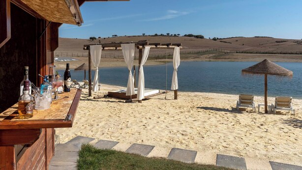 A beachside bar with a wooden counter, outdoor seating, and a view of the water. - Monte Vale Organic Farm (Castro Verde)