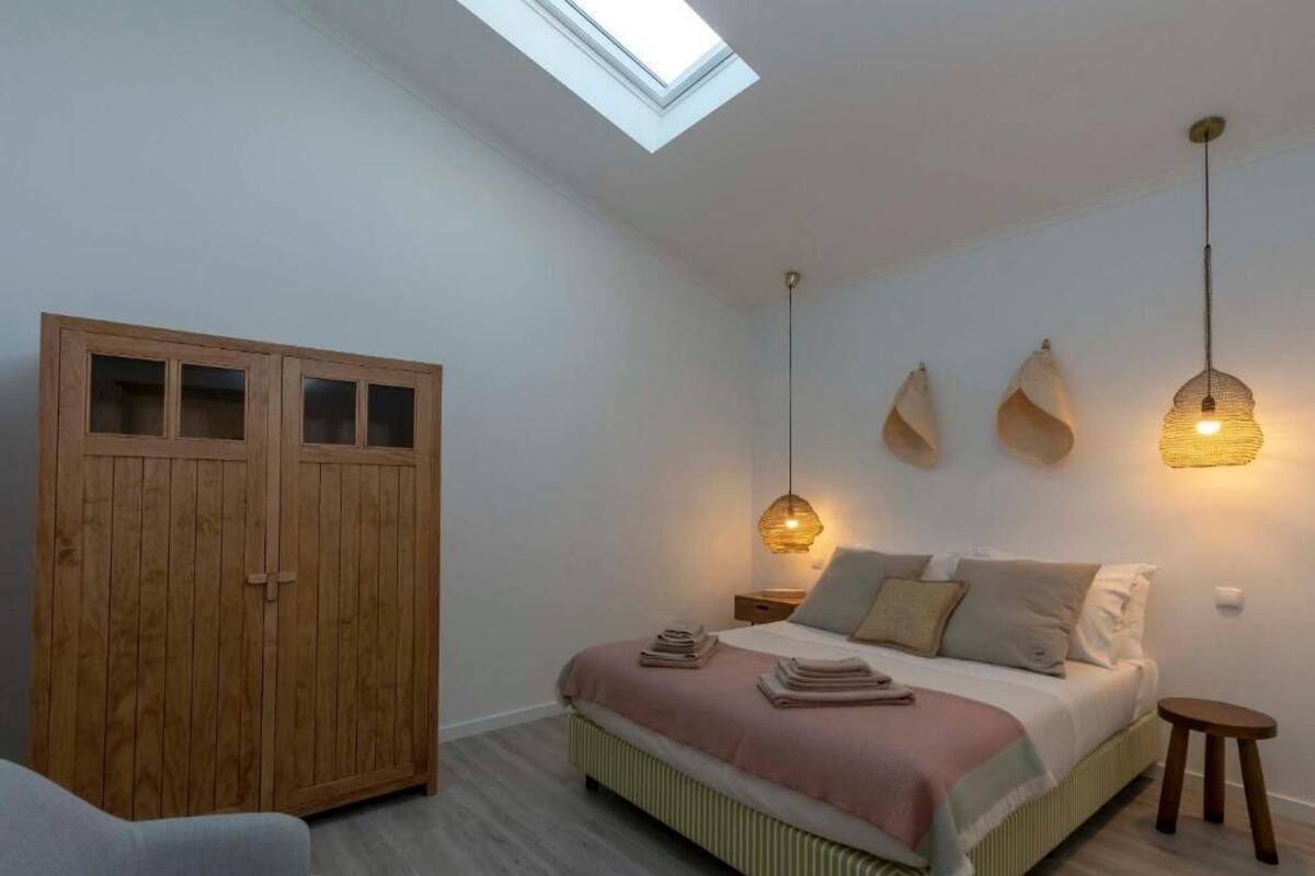 Ein Schlafzimmer mit Dachfenster, einem Bett mit Kissen, einem Nachttisch und einem Kleiderschrank.