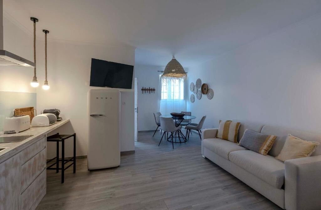 A modern kitchen with a built-in oven, a dining area with a round table and chairs, and a living room with a sofa and decorative wall art.