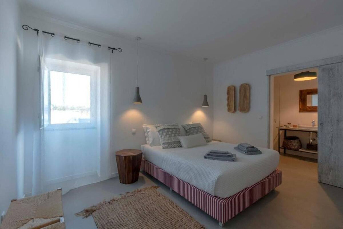 Ein Schlafzimmer mit einem Bett, Nachttischlampen, einem Fenster mit Vorhängen, einem Nachttisch und Blick auf ein Badezimmer.