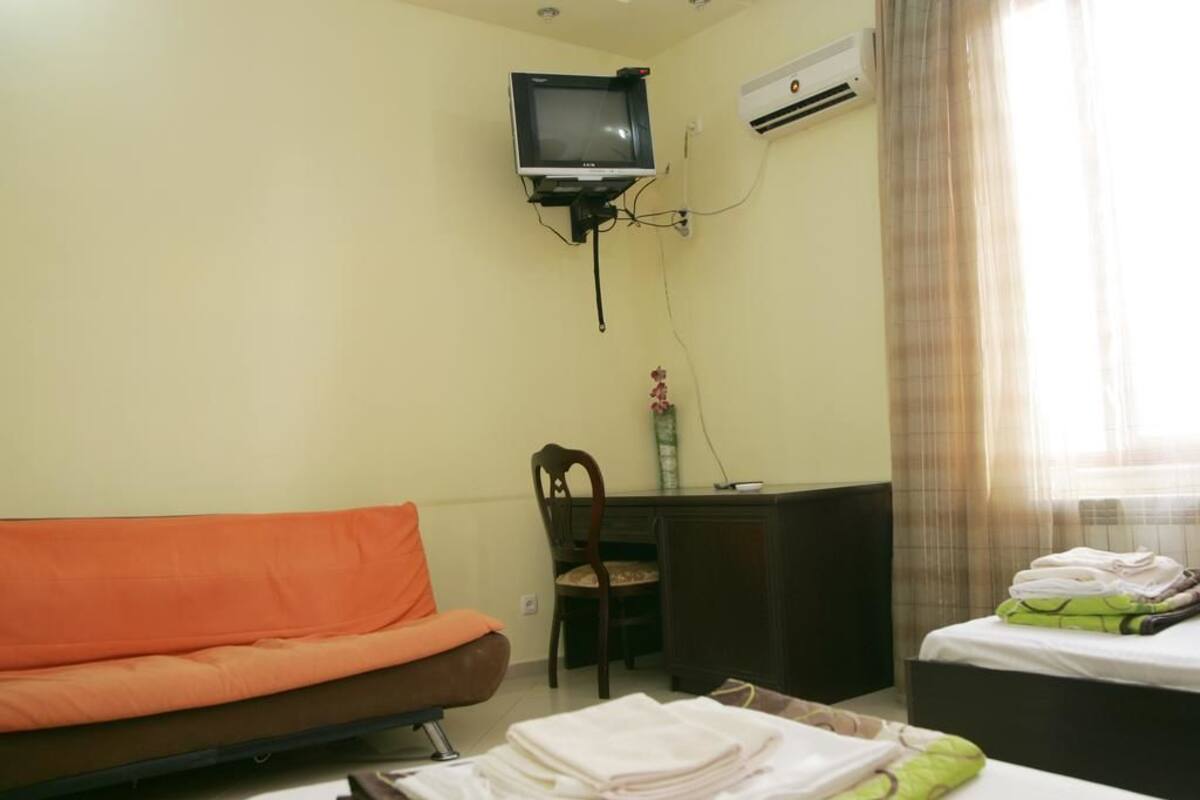 Una habitación con sofá, escritorio, televisión montada en la pared y cama con toallas ordenadas.