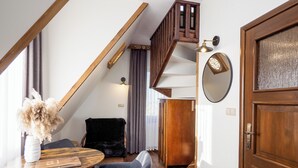 Een gezellige kamer met een houten trap, een ronde tafel met stoelen, een zwarte bank en een houten deur.