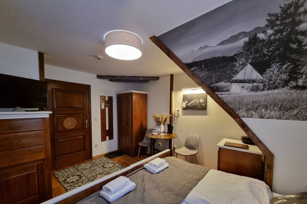 Une chambre d’hôtel comprenant un lit, une armoire en bois, un bureau, une chaise et un tableau représentant un paysage de montagne.