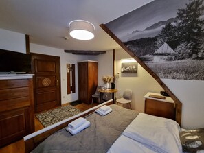 Hotelkamer met een bed, een houten garderobe, bureau, stoel en een schilderij van een berglandschap.