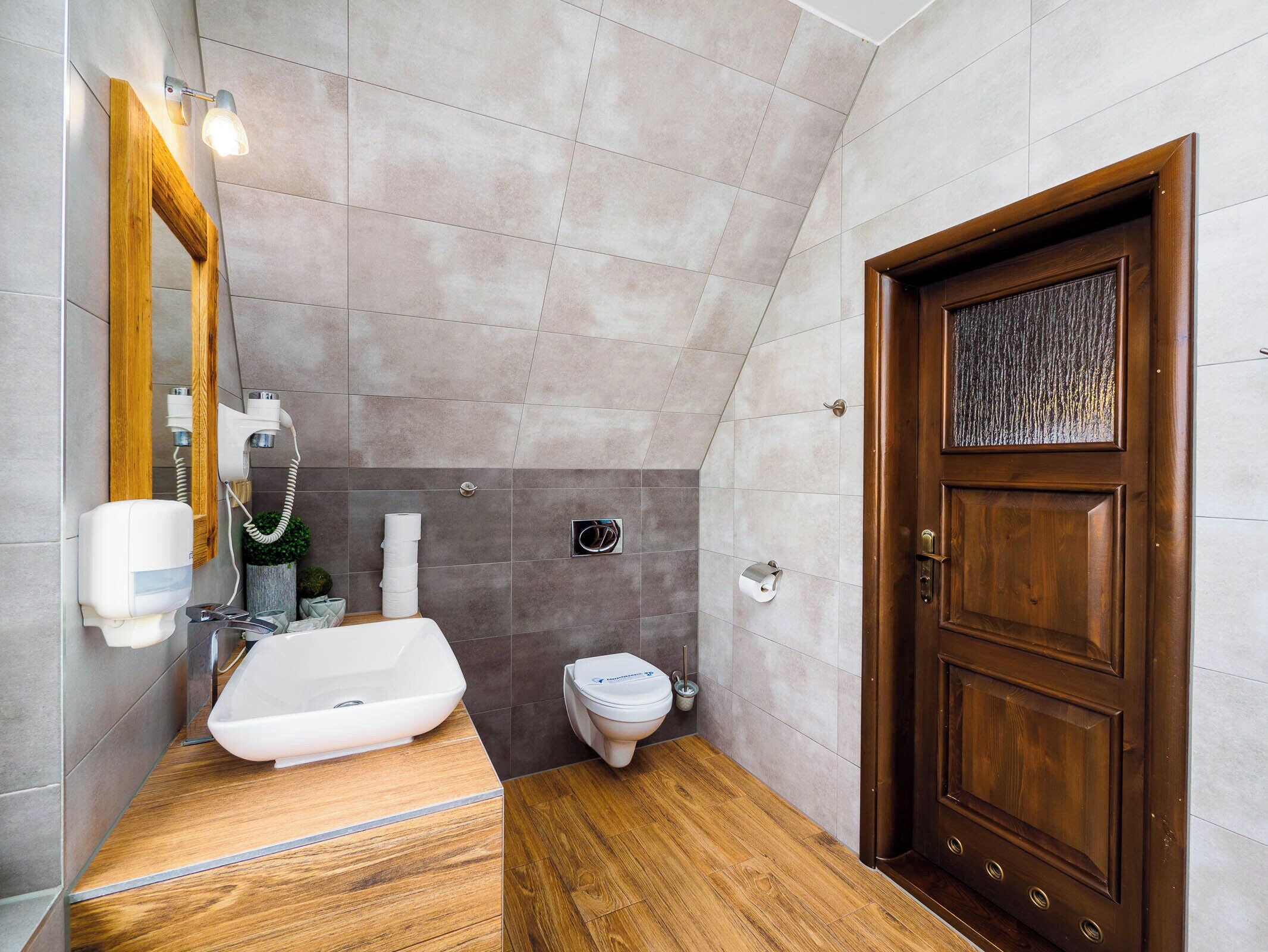 Une salle de bain moderne avec un meuble-lavabo en bois, un lavabo blanc, des toilettes et une porte en bois.