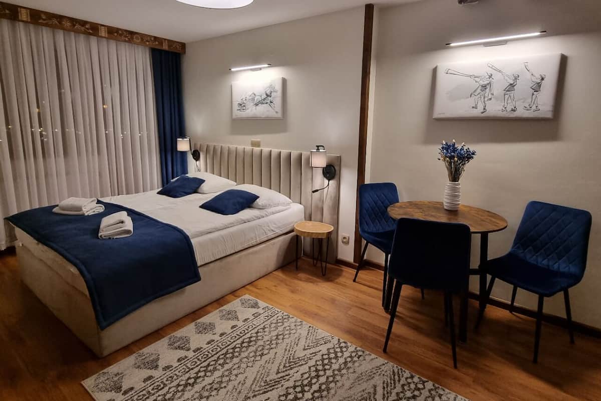 Une chambre d’hôtel avec un lit, une petite table ronde et deux chaises, une lampe de chevet et des œuvres d’art accrochées aux murs.