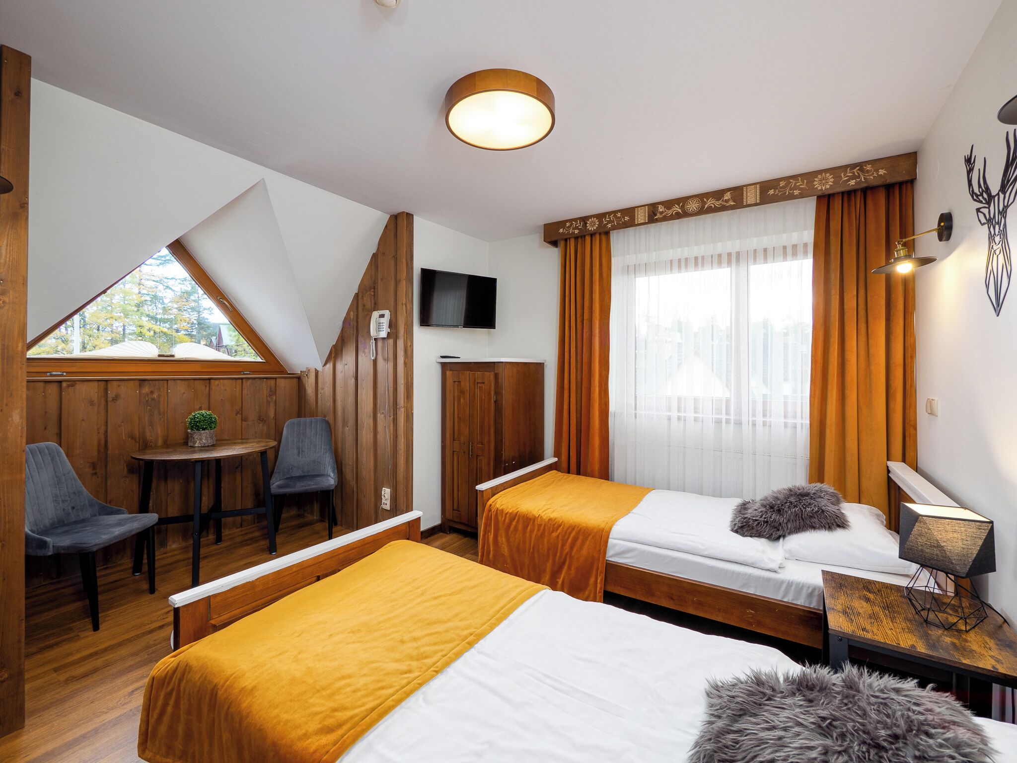 A hotel room with two beds, a TV, a small table with chairs, and a window with curtains.