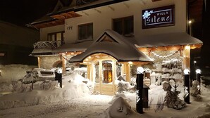 Een hotel met een met sneeuw bedekte buitenkant, een verlichte ingang en een bord waarop 'Villa Silene' staat.