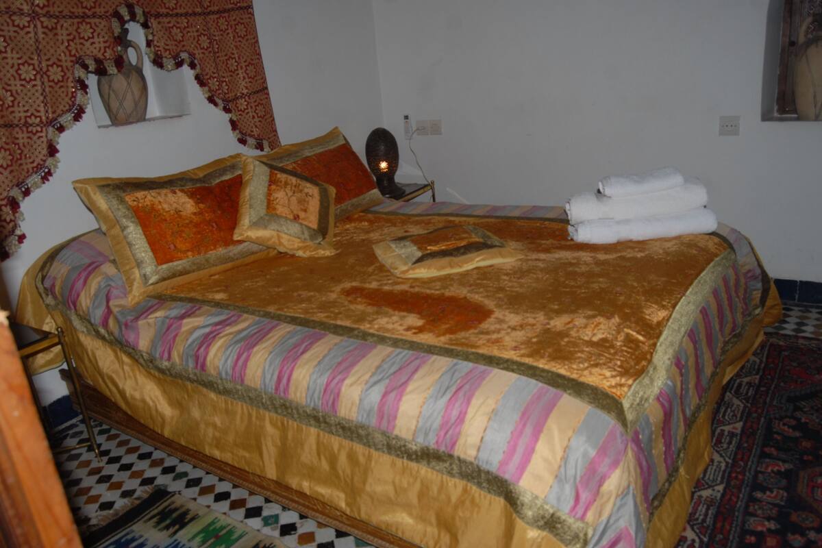 Una cama con una colcha a rayas, almohadas y una toalla doblada sobre un piso estampado.