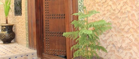 Una puerta de madera tradicional con una placa de número, una planta en maceta y un adorno en la pared.
