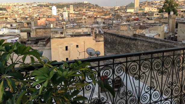 A cityscape with densely packed buildings, a prominent white tower, and a mosque with a green dome. - Dar La Bague De Kenza (Fes)