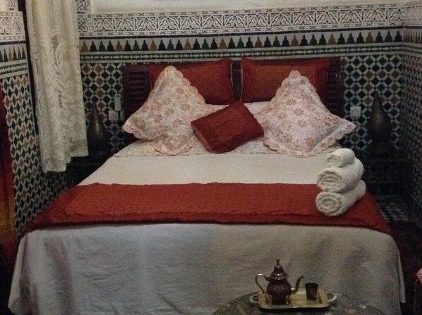 A bed with a red blanket, two pillows, and a tray with a teapot and cup. - Dar La Bague De Kenza (Fes)