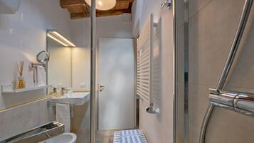 Un baño moderno con cabina de ducha de vidrio, un lavamanos blanco y un suelo de baldosas color beige.