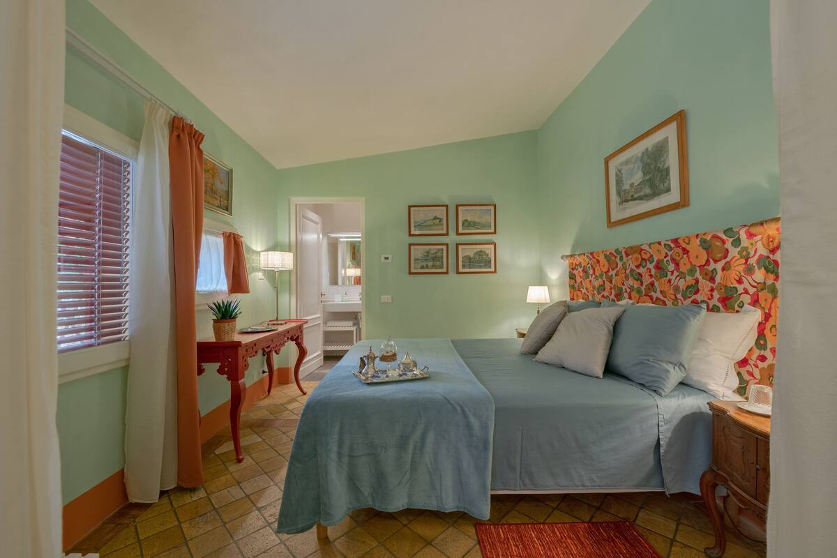 A bedroom with a bed, a desk, a chair, and a window with curtains.