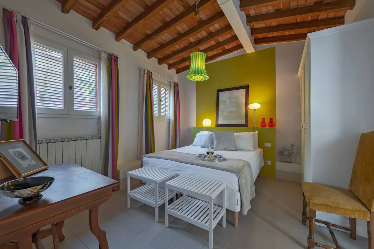 A bedroom with a wooden ceiling, a bed with white bedding, a bedside table with a bowl, and a chair.