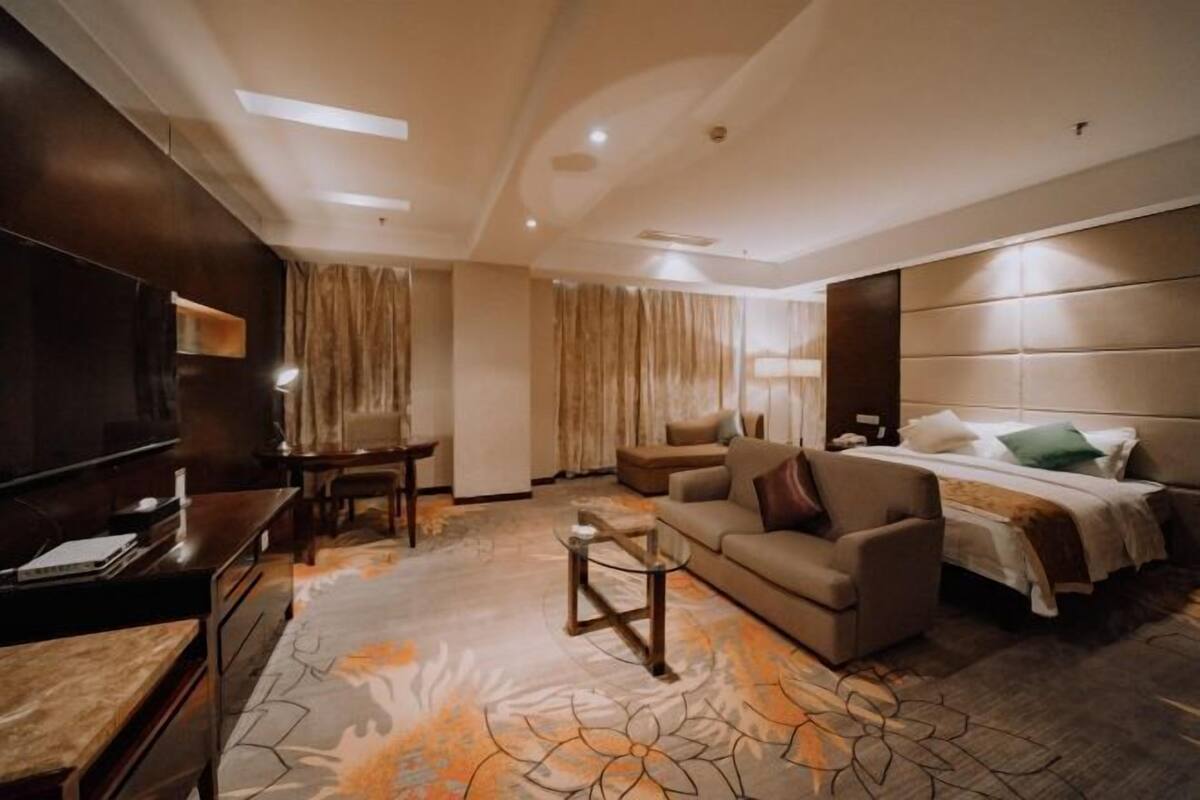 A hotel room with a bed, sofa, TV, desk, and curtains.