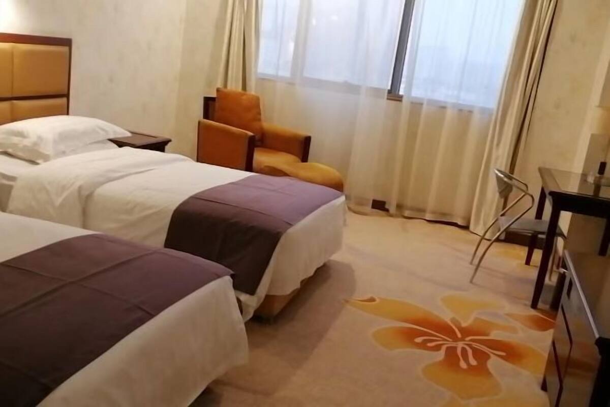A hotel room with two beds, a chair, a desk, and a window with curtains.