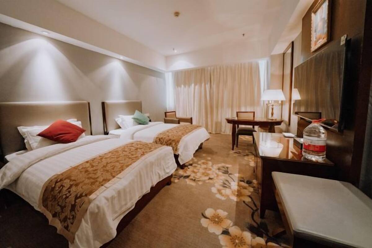 A hotel room with two beds, a desk, a chair, a lamp, and a water bottle.