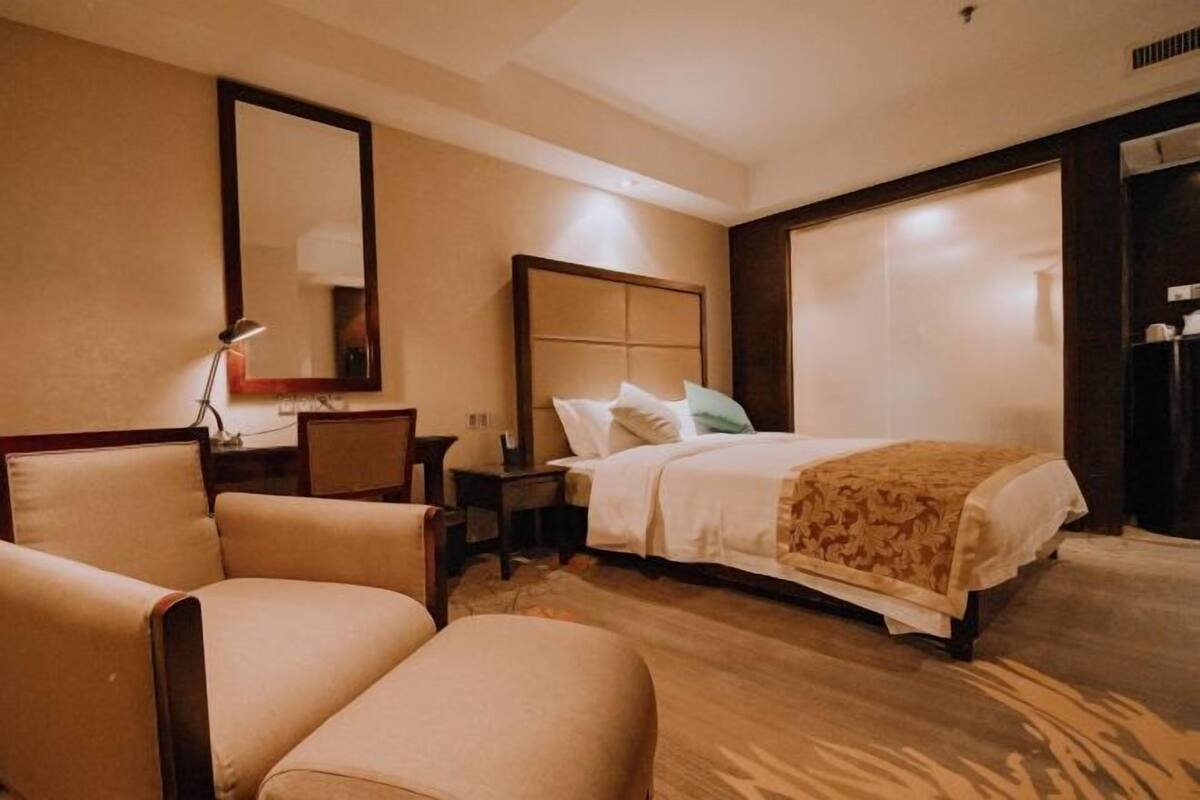 A hotel room with a bed, two armchairs, a desk, and a large mirror.