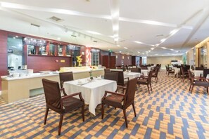 A hotel dining area with tables and chairs, a bar area with bottles, and a patterned carpet. - Linhai International Hotel (Funing)