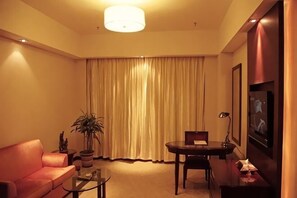 A hotel room with a sofa, a small table, a potted plant, a TV, and a large window with curtains. - Linhai International Hotel (Funing)