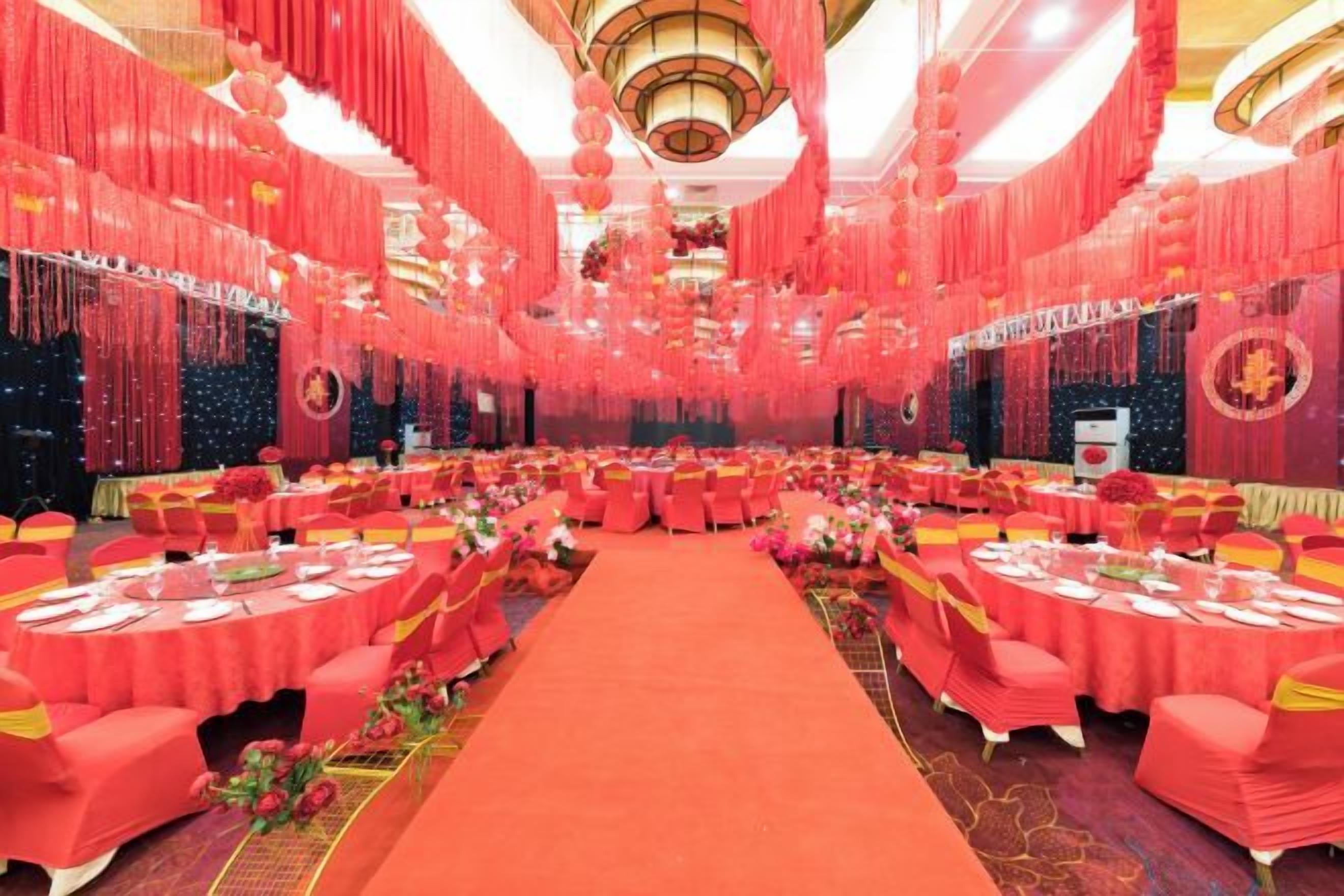 A banquet hall with round tables, red drapery, and a central aisle.