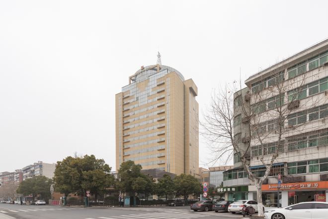A tall building with multiple floors and a flat roof, surrounded by other buildings and parked cars.