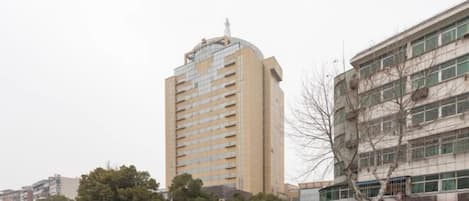 Un edificio alto con varios pisos y techo plano, rodeado de otros edificios y automóviles estacionados.