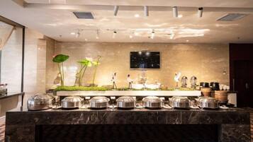 A buffet setup with multiple serving stations, a flat-screen TV mounted on the wall, and a decorative plant arrangement.