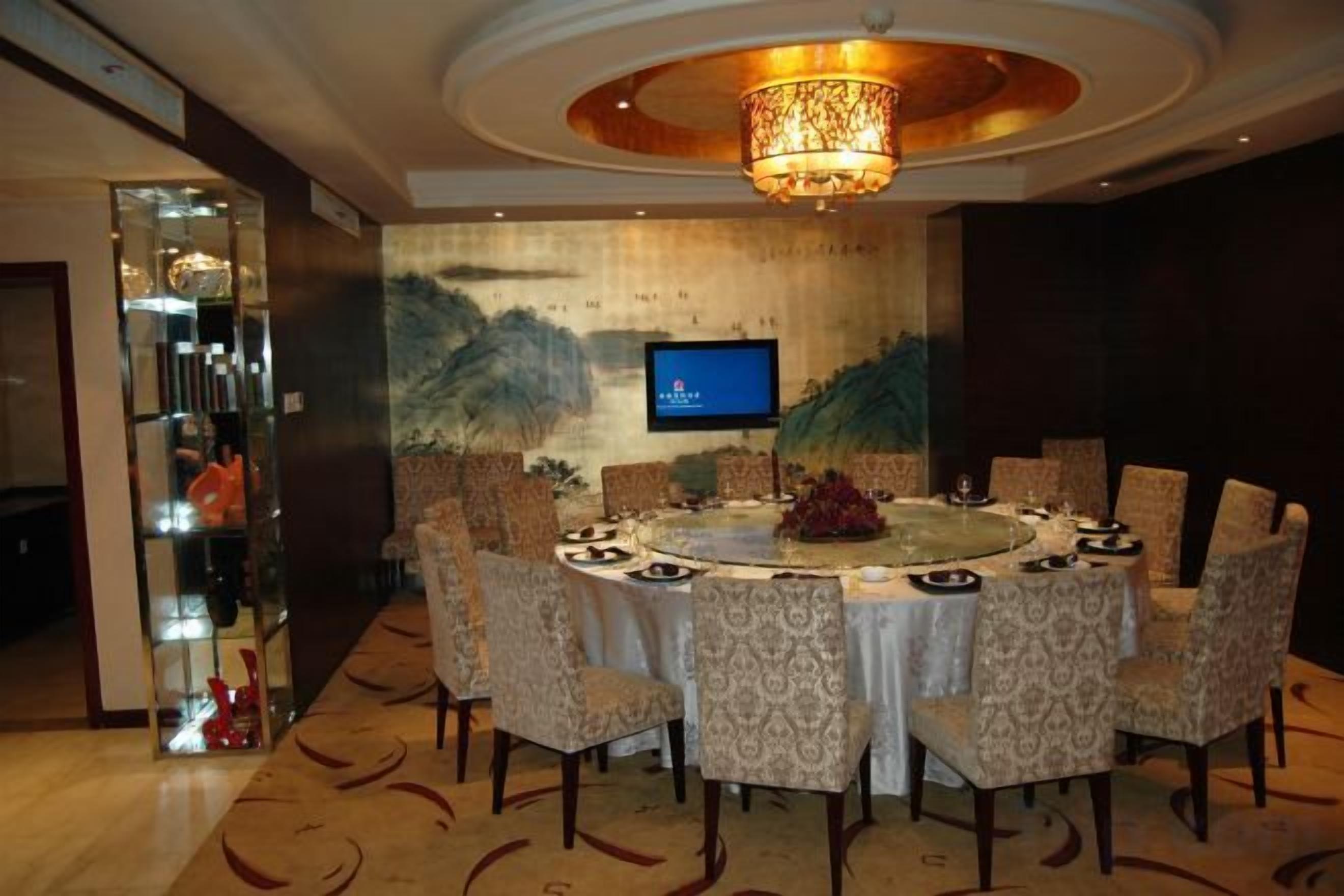 A round dining table with chairs, a chandelier, and a television on the wall.