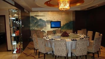 A round dining table with chairs, a chandelier, and a television on the wall.