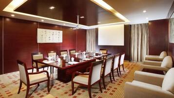 A conference room with a long table, chairs, a projector screen, and a carpeted floor.