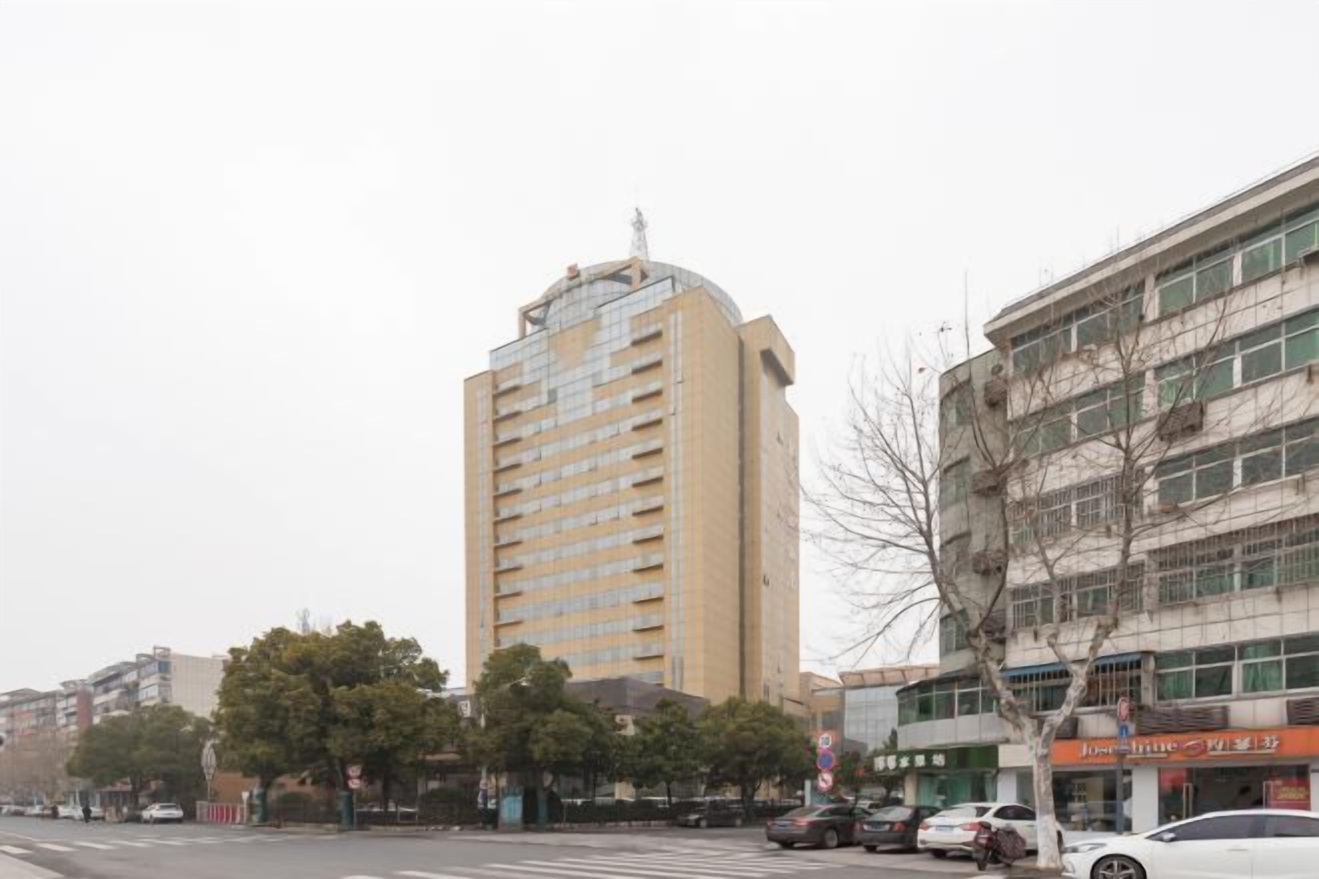 Un immeuble à plusieurs étages doté d’une façade plate, avec un passage piéton devant et des voitures garées le long de la rue.