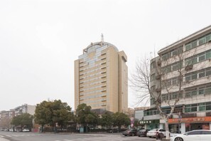 A multi-story building with a flat facade, a crosswalk in front, and parked cars along the street. - Linhai International Hotel (Funing)